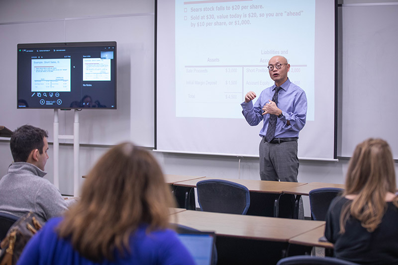 Professor Bing Yu gives MBA 650 class lecture while three visible students take notes