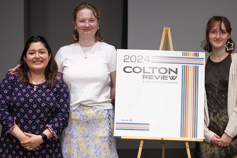 Three students smiling next to a sign that says "2024 Colton Review".